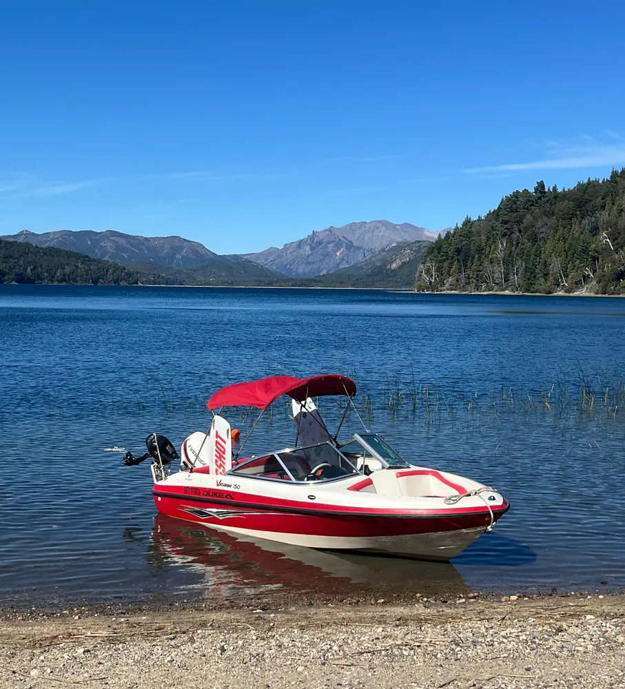 Embarcación roja y blanca junto a la costa, con el lago y las montañas de fondo