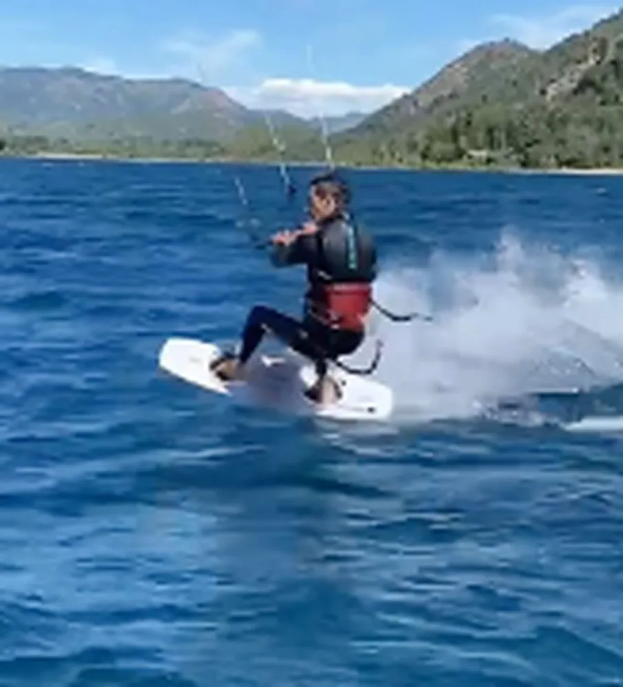 Persona haciendo kite sobre el lago con montañas de fondo