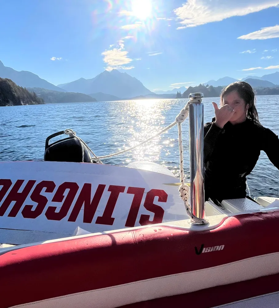 Persona con traje de neoprene junto a una tabla de wakeboard y la embarcación
